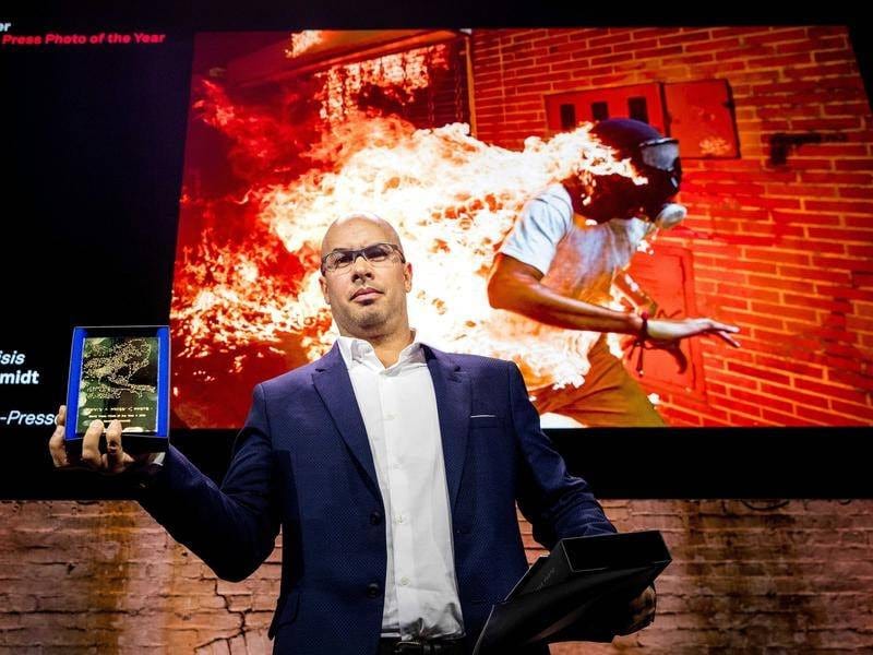 Ronaldo Schemidt holds an award while standing in front of a projection of his winning photo.