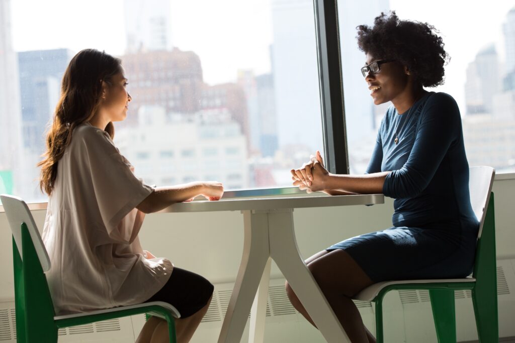 Image Description: Two professionally-dressed women sit at a table for an interview.