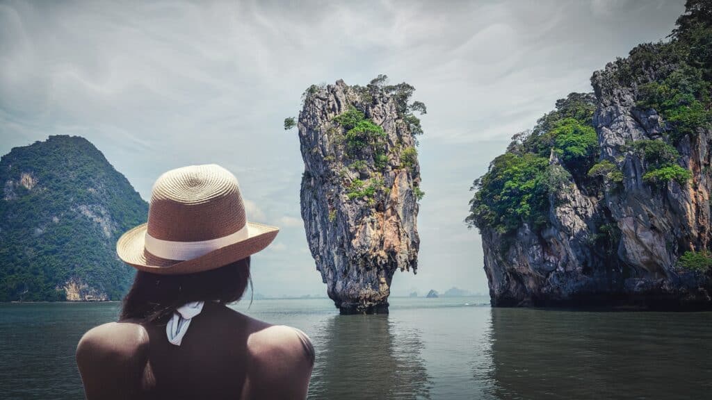 A vacationing woman looks out at tall sea stacks in a bay.