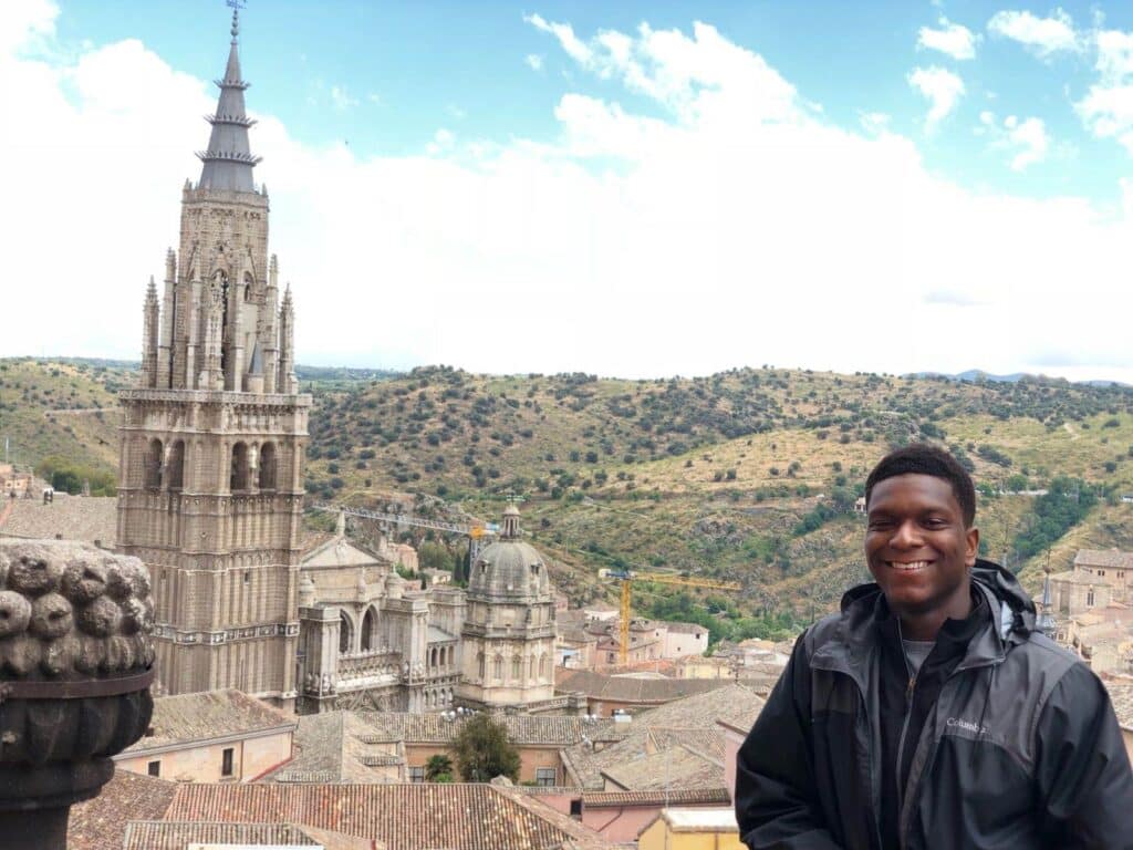 The author stands in front of a view of a cathedral tower and the Spanish countryside