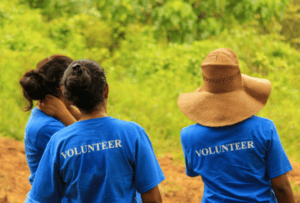 A picture containing three people, outdoor, wearing shirts that say "VOLUNTEER" on them.